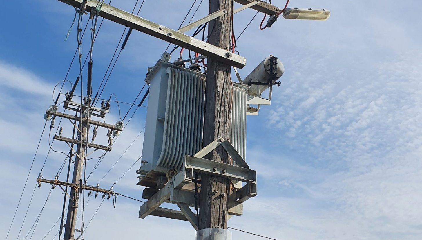 Full-resolution crop of the power pole transformer against a blue sky.